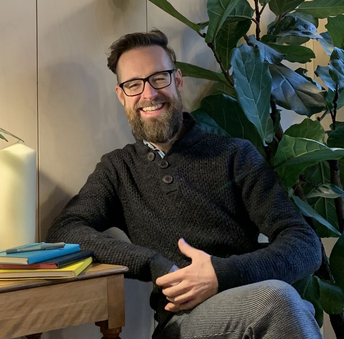 Dan Simpson smiling, seated beside a stack of notebooks and a fig plant